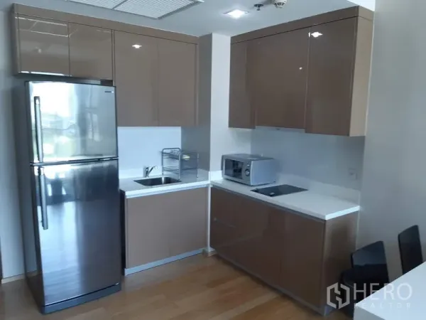 Condominium for rent in Khlong Toei, Bangkok - Modern built-in kitchen with glossy cabinets, stainless refrigerator, electric hob and microwave on wood floors.