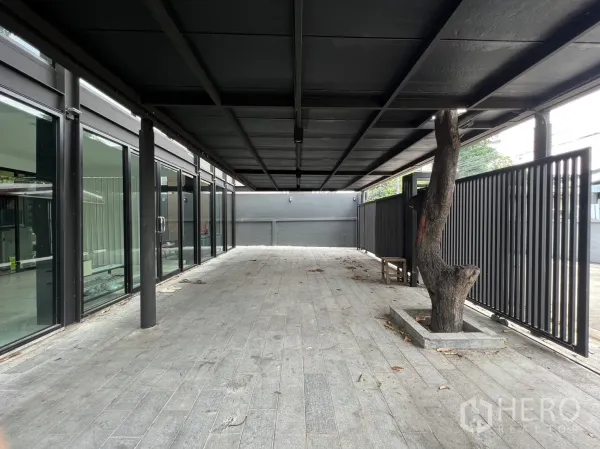 Detached House for rent or sale in Phra Khanong, Bangkok - Long covered terrace and parking area with slatted fence and integrated tree planter.