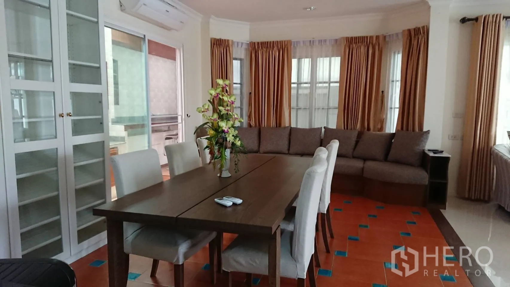 Detached House for rent in Mueang Samut Prakan, Samut Prakan - Dining area with a six-seat table, display cabinet and corner sofa beside bay windows.