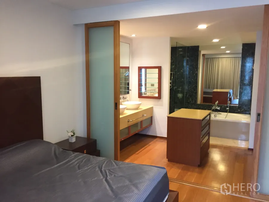 Condominium for rent in Khlong Toei, Bangkok - Master bedroom with ensuite bathroom featuring a soaking tub, vanity, and warm wood floors.