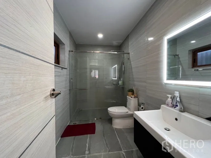 บ้าน ขายในChatuchak, Bangkok - ห้องน้ำสมัยใหม่พร้อมตู้กระจกกั้นอาบน้ำ กระจกไฟ และผนังกระเบื้องโทนเทา.