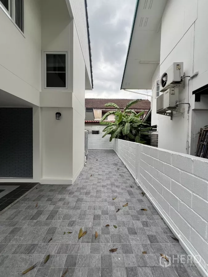 Detached House for rent in Saphan Sung, Bangkok - Side walkway with gray tiles beside the house and low white wall.