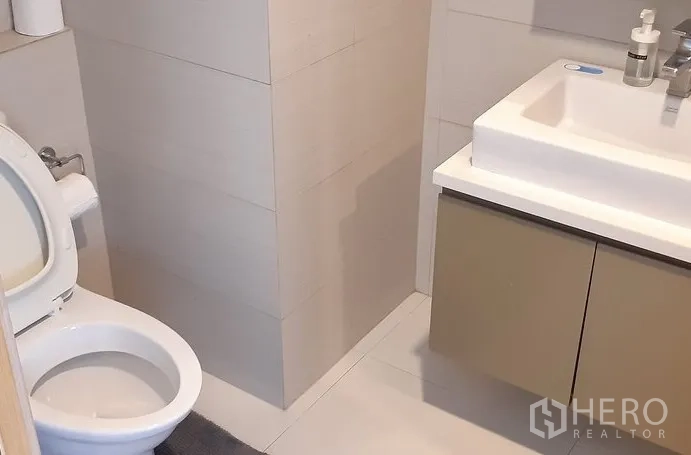 Condominium for rent in Khlong Toei, Bangkok - Second bathroom with vanity and toilet in neutral tiles.