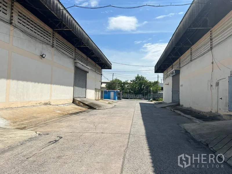 货栈 出租在Mueang Samut Prakan, Samut Prakan - 两栋仓库之间的宽阔车道，设有装卸坡道与金属卷帘门。