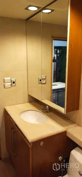Condominium for sale in Watthana, Bangkok - Vanity area with large mirrored cabinet, built-in sink and warm downlights in the bathroom.