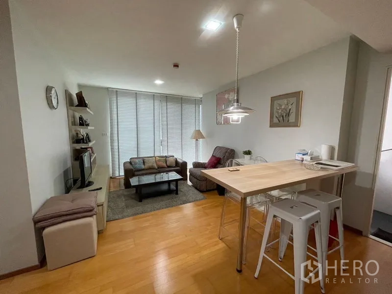 Condominium for sale in Khlong Toei, Bangkok - Bright open-plan living room with sofa set, TV shelf and a breakfast bar beside floor-to-ceiling blinds.
