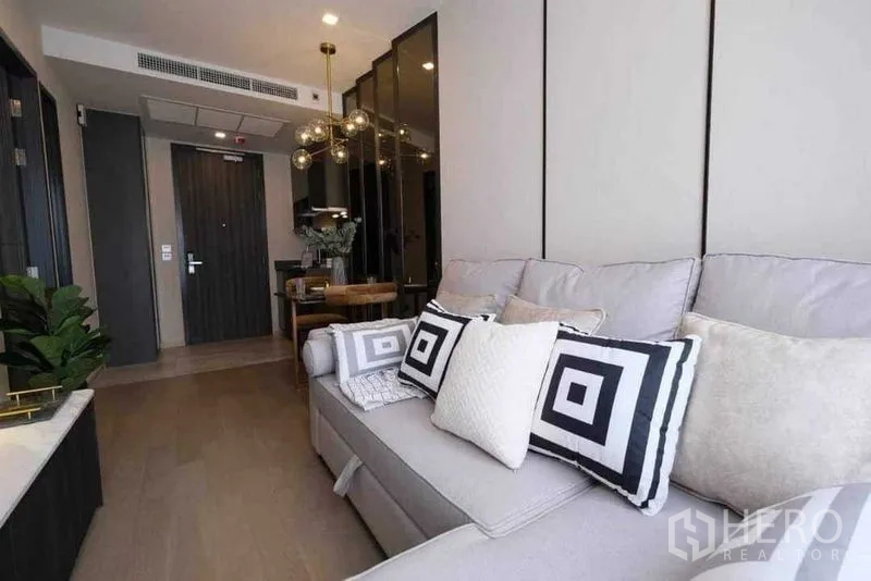 公寓 出租在Watthana, Bangkok - 灰色沙发配几何抱枕，对面是入户门与餐区