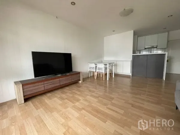 Condominium for rent in Watthana, Bangkok - Open-plan living room with wood floors, TV console and compact kitchen in an Ekkamai condo.