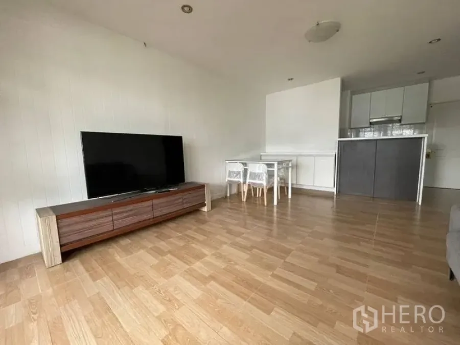 Condominium for rent in Watthana, Bangkok - Open-plan living room with wood floors, TV console and compact kitchen in an Ekkamai condo.