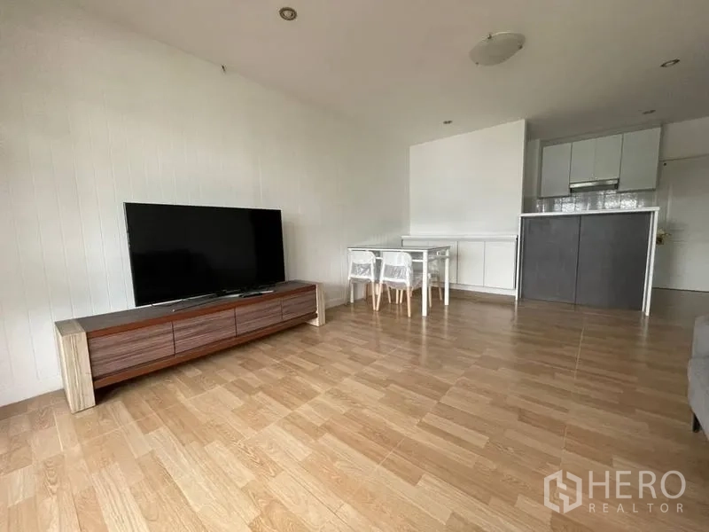 Condominium for rent in Watthana, Bangkok - Open-plan living room with wood floors, TV console and compact kitchen in an Ekkamai condo.