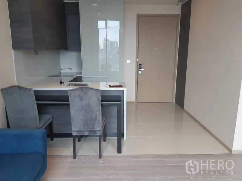 Condominium for rent or sale in Watthana, Bangkok - Compact open kitchen with stone-top island and dining chairs near the entrance.