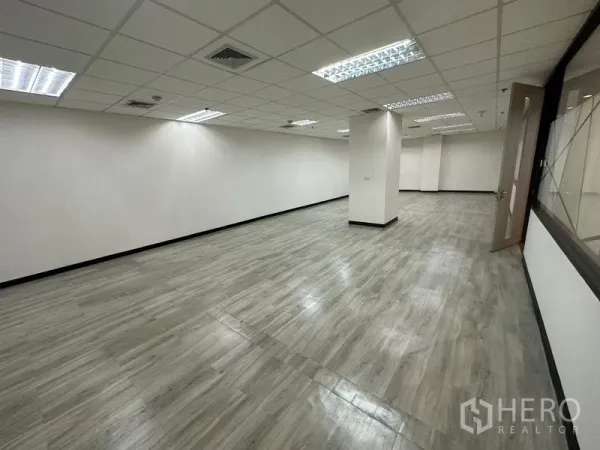 办公空间 出租 - 大开间办公室，格栅吊顶灯，白墙与灰色地板，局部立柱。