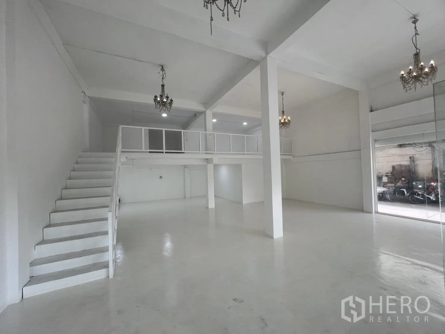 Retail Space for rent in Khlong Toei, Bangkok - Spacious retail hall with staircase to mezzanine, support columns and floor-to-ceiling windows.