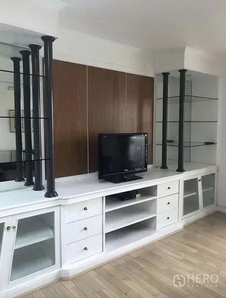 Condominium for rent in Khlong Toei, Bangkok - Living area media wall with TV, white cabinets and glass shelving accents.