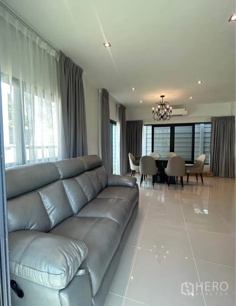 Semi-detached House for rent in Bang Phli, Samut Prakan - Wide view of living area toward dining space with long leather sofa and full-height curtains.