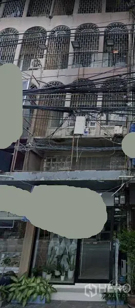 Shophouse for rent in Watthana, Bangkok - Multi-storey shophouse facade in Thonglor with arched window grilles, glass storefront entrance, potted plants, and overhead utility cables.
