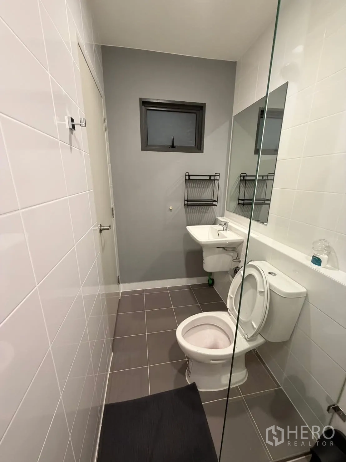 联排别墅 for rent in Bang Phli, Samut Prakan - 卫生间灰白色瓷砖，挂墙式洗手盆、坐便与小窗，玻璃隔断。