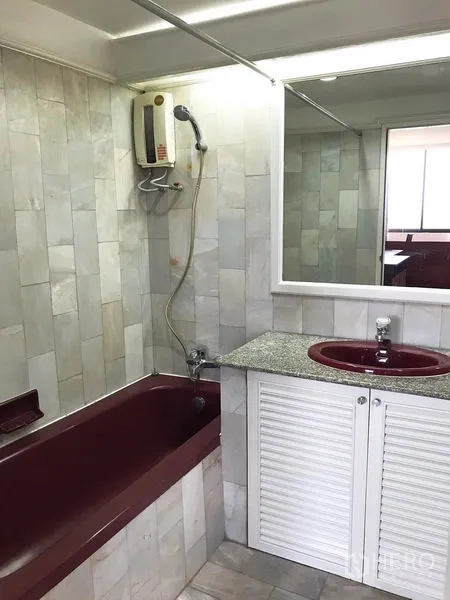 Condominium for rent or sale in Watthana, Bangkok - Bathroom with burgundy bathtub and sink, electric water heater and large mirror.