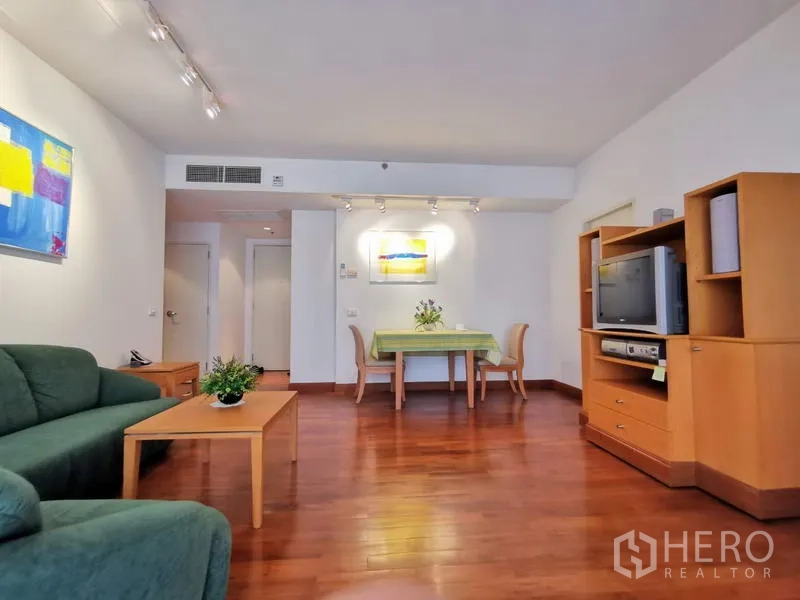 Condominium for rent in Pathum Wan, Bangkok - Bright living and dining area with hardwood floors, green sofa, wooden media cabinet and track lighting.