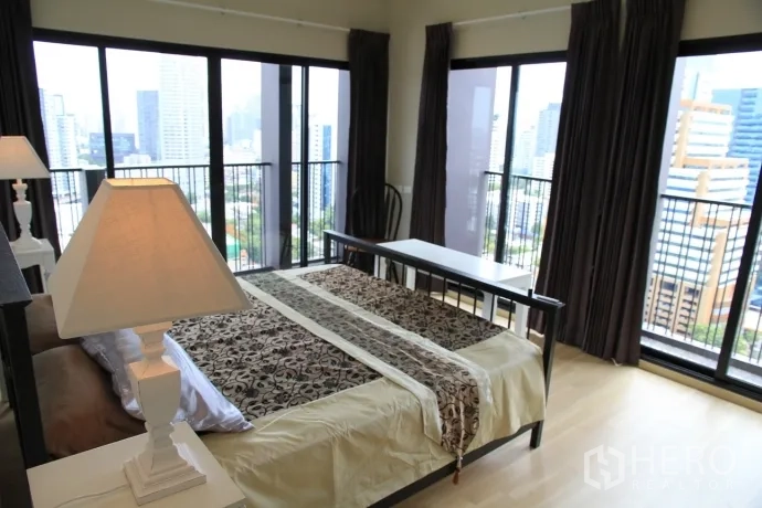 Condominium for rent or sale in Watthana, Bangkok - Corner bedroom with floor-to-ceiling windows, wooden floor and expansive city skyline views.