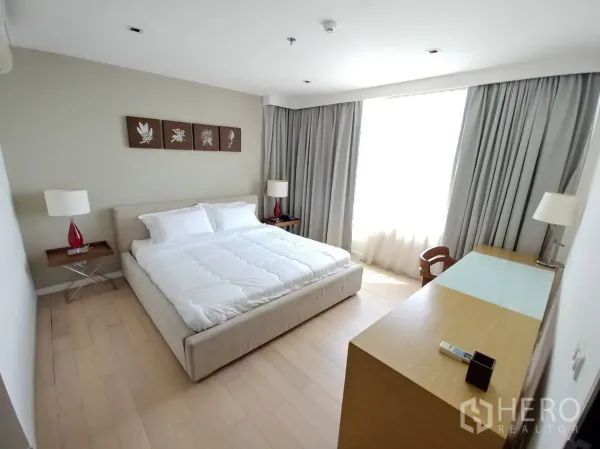 公寓 出租在Watthana, Bangkok - 主卧明亮，特大床、床头灯、窗边书桌与浅木地板。