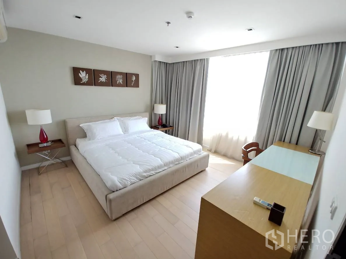 公寓 出租在Watthana, Bangkok - 主卧明亮，特大床、床头灯、窗边书桌与浅木地板。