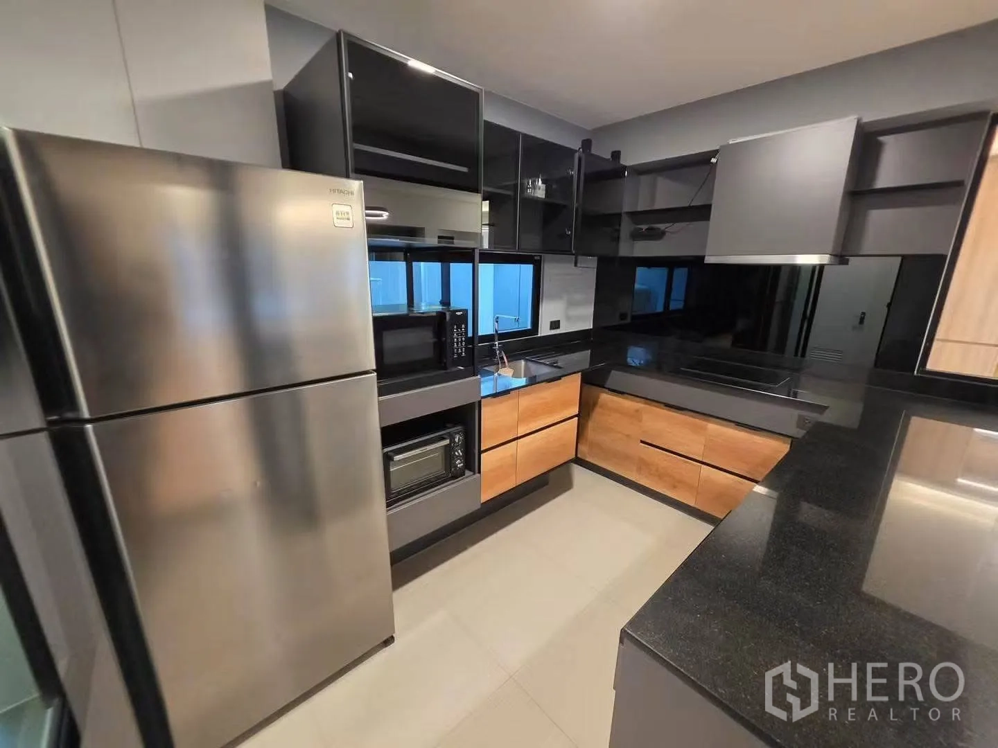 Townhouse for rent in Bang Phli, Samut Prakan - U-shaped kitchen with black stone countertops, wood cabinets, and stainless appliances.