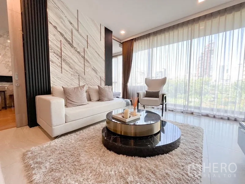 Condominium for rent in Watthana, Bangkok - Living room with marble accent wall, large curtain-lined windows, and city outlook.
