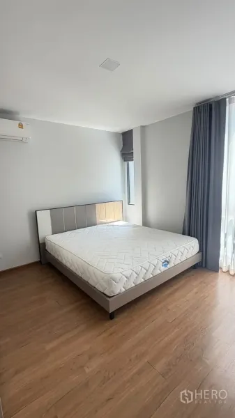 Townhouse for rent in Bang Phli, Samut Prakan - Spacious bedroom with a double bed, large windows, curtains, and wood flooring.