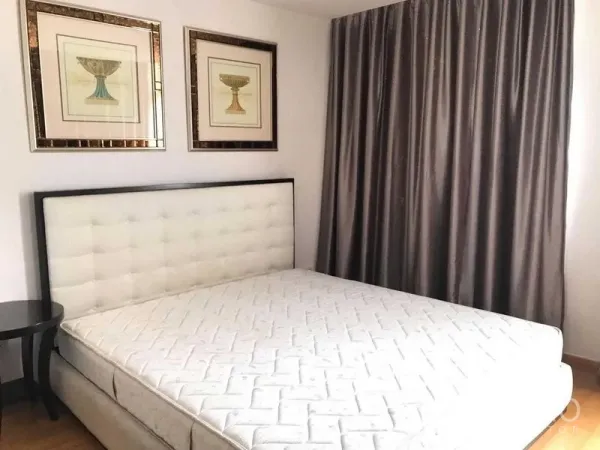 Condominium for rent in Khlong Toei, Bangkok - Cozy bedroom with upholstered headboard, framed artwork, and blackout curtains.