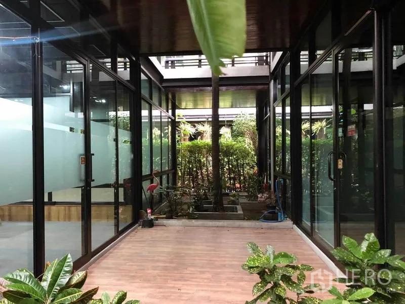 Office Space for rent in Bang Na, Bangkok - Indoor courtyard corridor with glass walls, wood-look flooring and landscaped greenery.