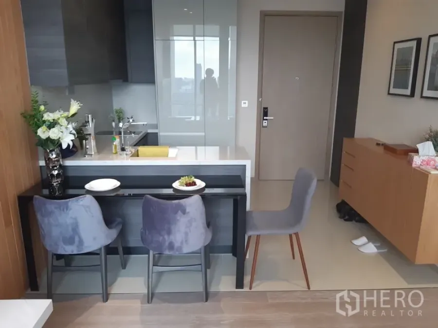 公寓 出租或出售在Watthana, Bangkok - 带吧台的用餐岛台，吧椅面向开放式小厨房与入户收纳柜。