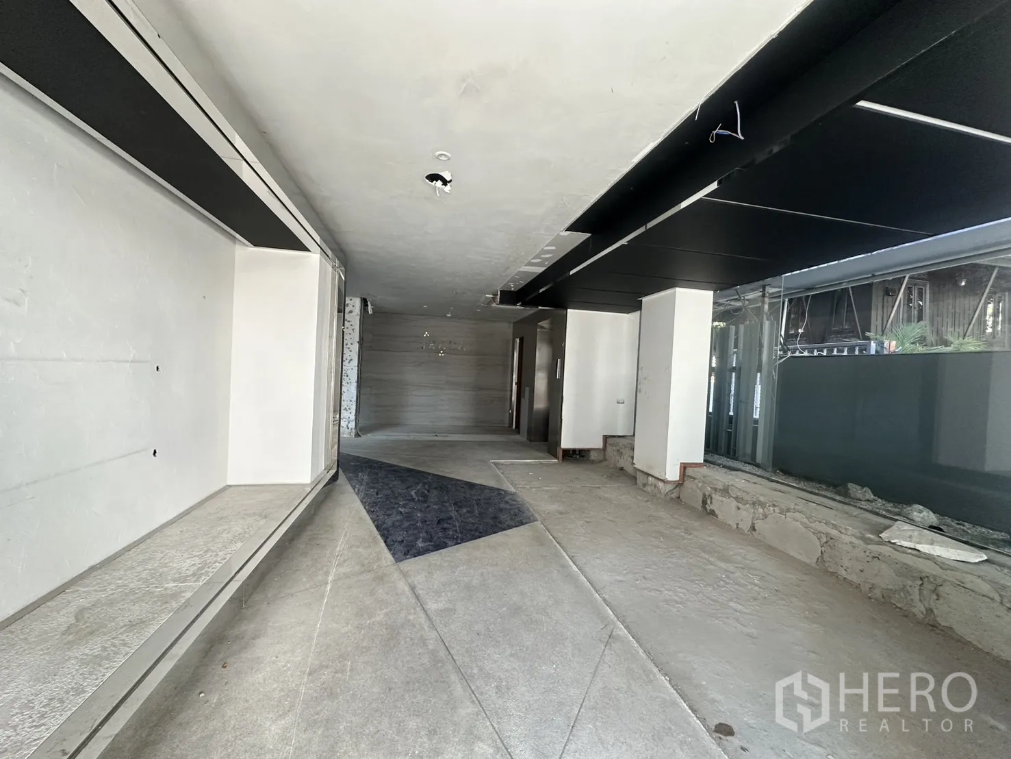 พื้นที่ขายของ for rent in Watthana, Bangkok - พื้นที่ค้าปลีกชั้นล่างกำลังปรับปรุง พื้นคอนกรีต เพดานโทนเข้ม และกระจกด้านข้างบานใหญ่.