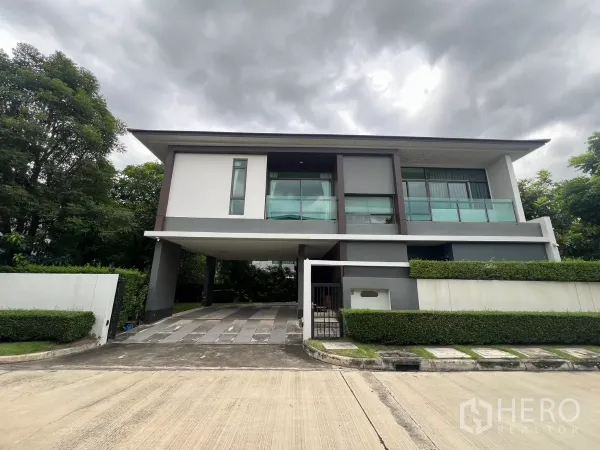 บ้าน ให้เช่าในBang Kapi, Bangkok - บ้านเดี่ยวสองชั้นสไตล์โมเดิร์นมุมถนน มีระเบียงกระจกและโรงจอดรถ รายล้อมด้วยแนวรั้วต้นไม้