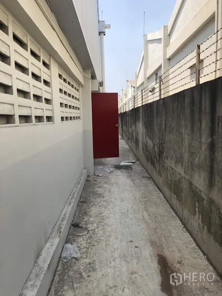 Factory for rent in Khlong Luang, Pathum Thani - Rear service walkway with red emergency exit door and security wall.