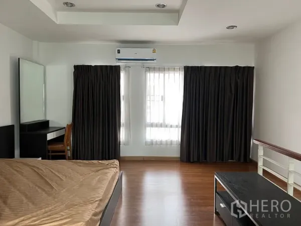 Townhouse for rent in Saphan Sung, Bangkok - Master bedroom with large windows, dark curtains and an air conditioner.