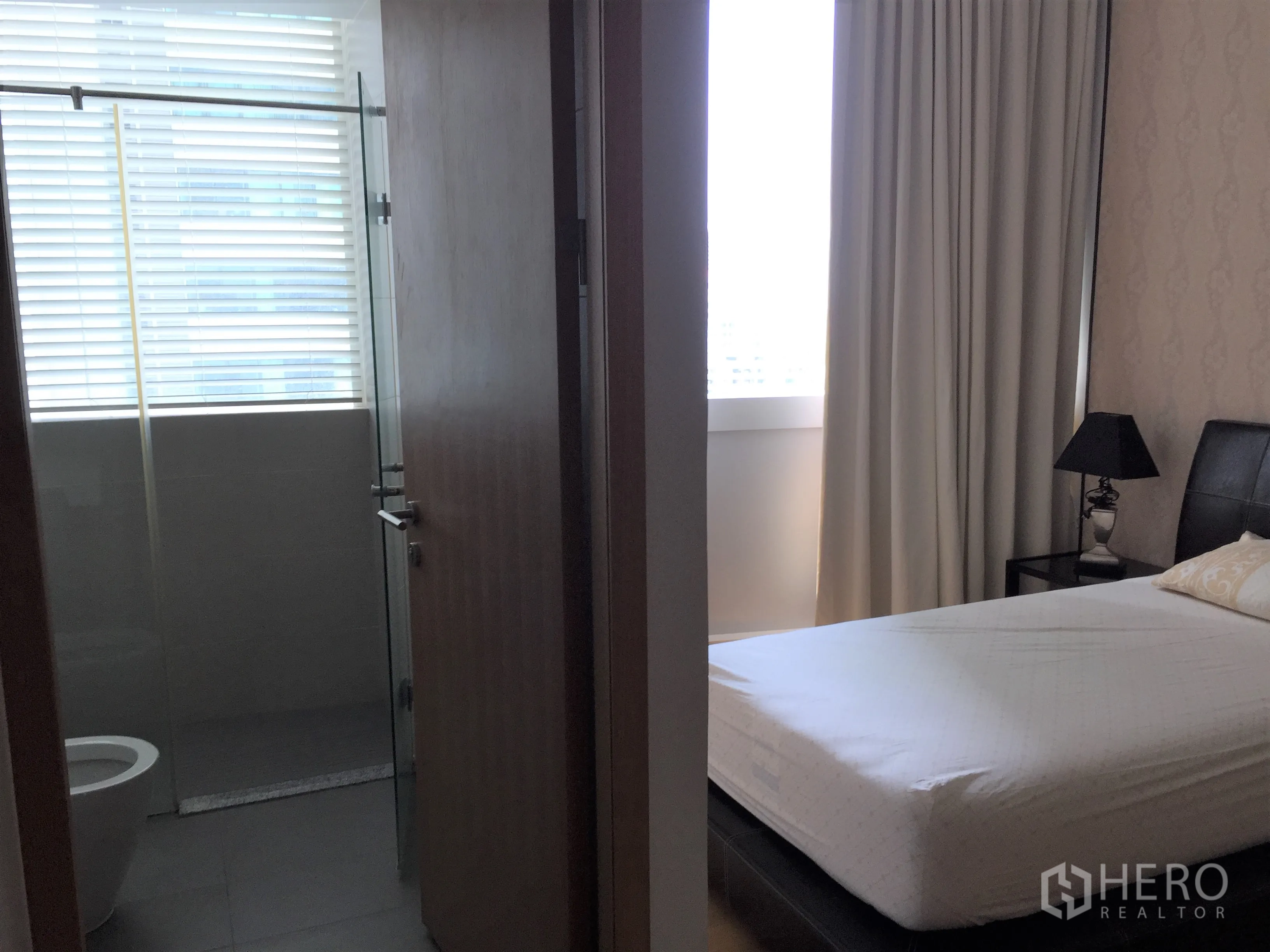 Condominium for rent or sale in Khlong Toei, Bangkok - Secondary bedroom and bathroom with glass shower, large window with blinds and neutral decor.