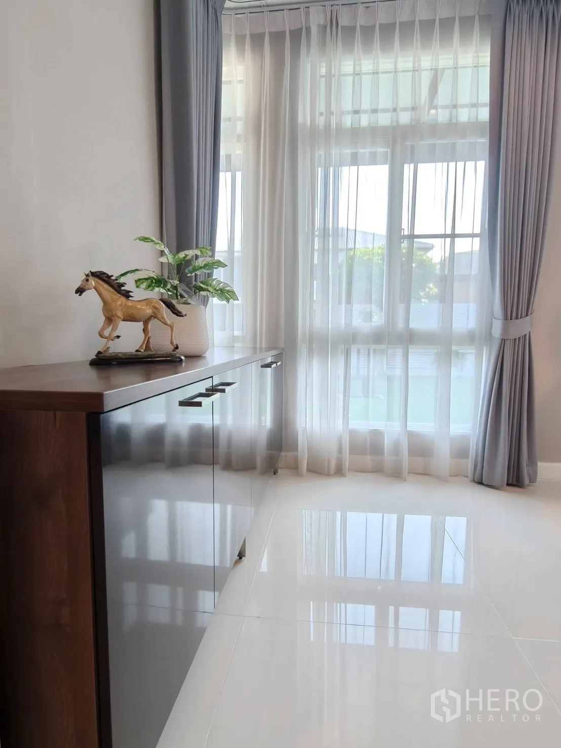 บ้านเดี่ยว for rent or sale in Bang Phli, Samut Prakan - มุมบ้านสว่างพร้อมตู้วางของ กระถางต้นไม้ และม่านโปร่งบานสูง.