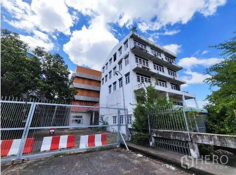 Factory for rent in Phra Samut Chedi, Samut Prakan - Gated entrance to a standalone industrial complex with a multi‑storey office building under blue skies.