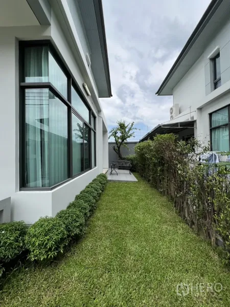 Detached House for rent in Bang Kapi, Bangkok - Side garden with green lawn, shrubs and a bay window along the house.