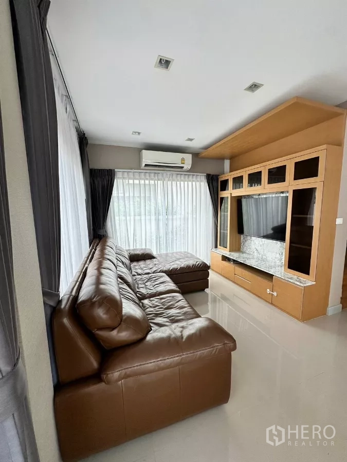 Detached House for rent in Saphan Sung, Bangkok - Bright living room with brown leather sectional sofa and built-in TV wall unit.