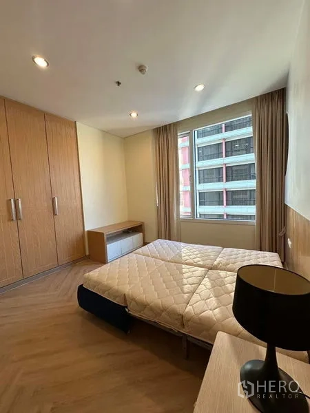 Condominium for rent in Bang Rak, Bangkok - Bedroom with large wardrobe, window, and timber floors.