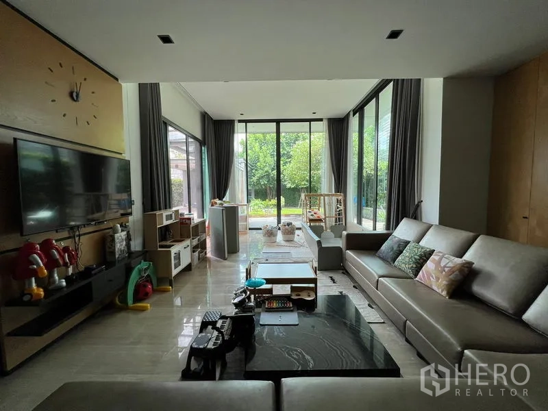 Detached House for sale in Bang Kapi, Bangkok - Living room with large sofas, TV wall and floor-to-ceiling glass facing the yard.