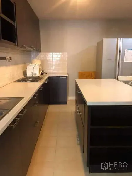 Condominium for sale in Yan Nawa, Bangkok - Galley-style kitchen with dark cabinetry, white countertop island and gas cooktop.