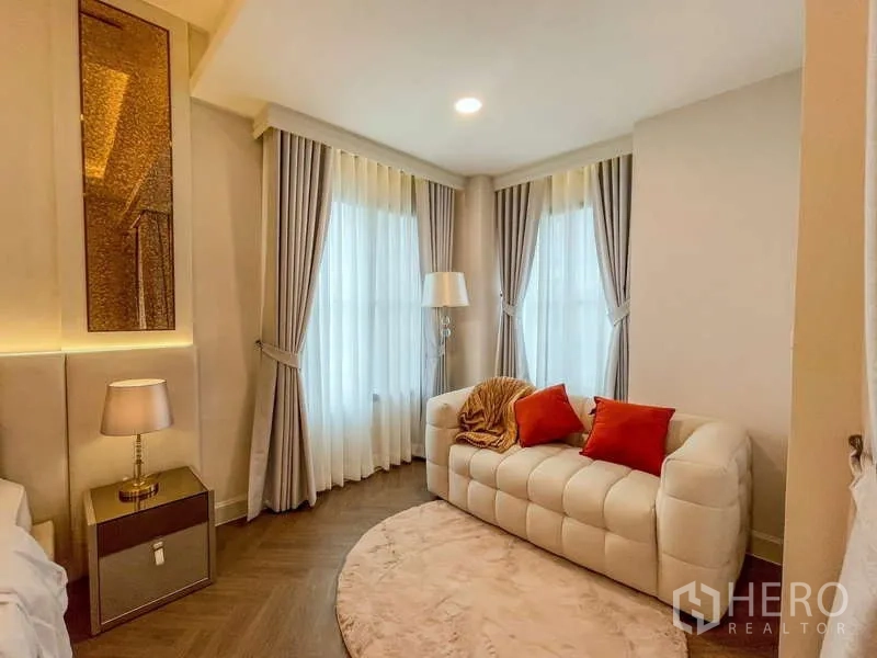Detached House for rent in Saphan Sung, Bangkok - Cozy sitting nook with a tufted white sofa, floor lamp and sheer drapes.