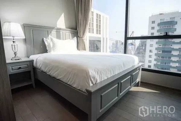 公寓 出租或出售在Watthana, Bangkok - 次卧配灰色床架，转角大窗，城市景观。