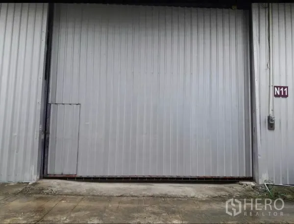 Warehouse for rent in Lam Luk Ka, Pathum Thani - Close-up of gray steel sliding warehouse door with side access door and unit sign N11.