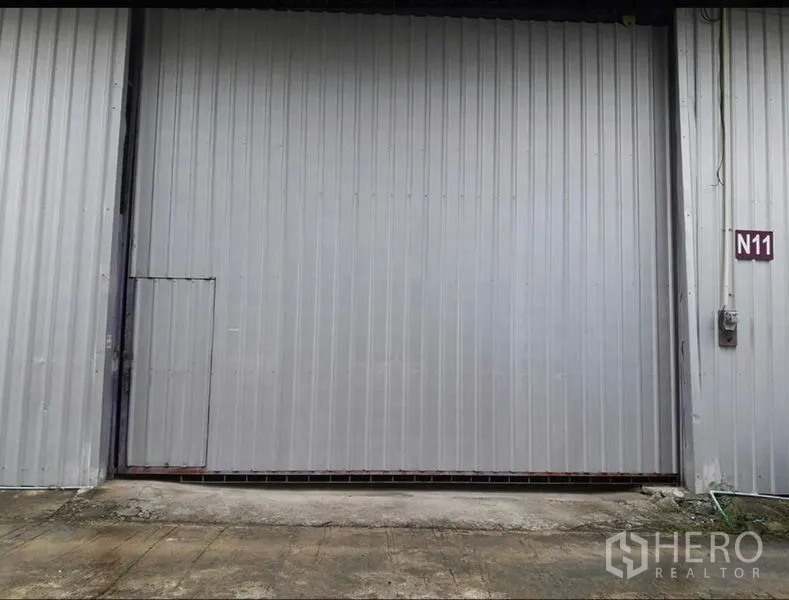 Warehouse for rent in Lam Luk Ka, Pathum Thani - Close-up of gray steel sliding warehouse door with side access door and unit sign N11.