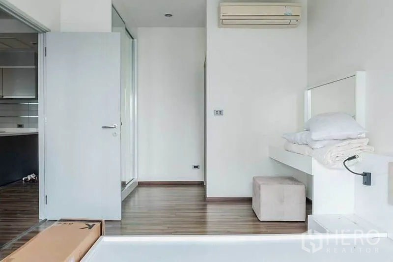 Condominium for rent in Khlong Toei, Bangkok - Bedroom with wood flooring, platform bed, wall-mounted air conditioner and doorway to the kitchen.