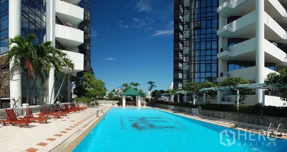 Condominium for rent in Watthana, Bangkok - Outdoor condominium swimming pool with sun loungers between high-rise buildings.